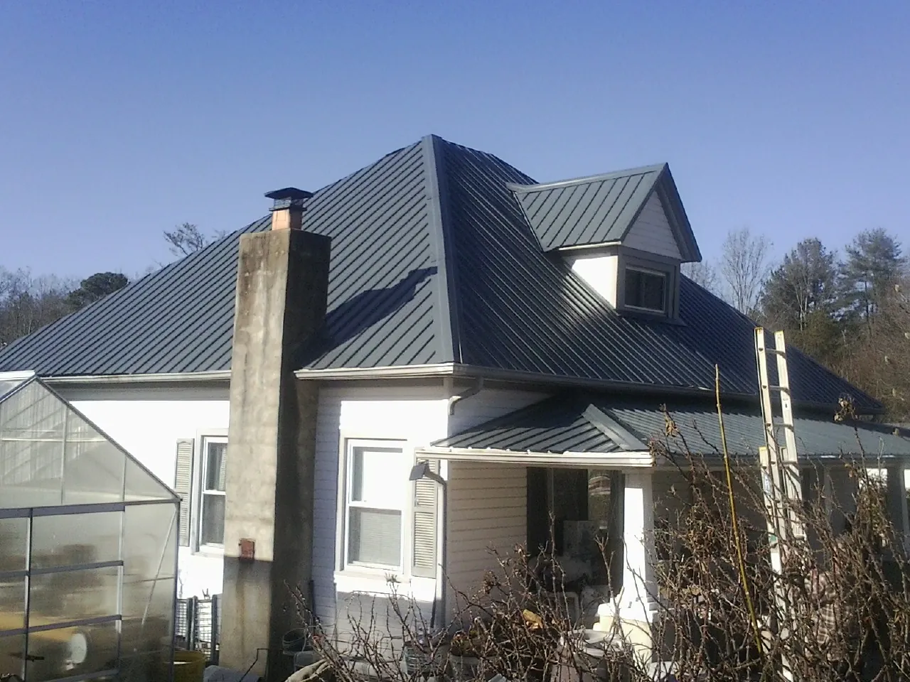 Dark blue standing seam metal roof on a white farmhouse with dormer — Slate & Tile Roof Repair by Roofing Brothers in Picture Rocks