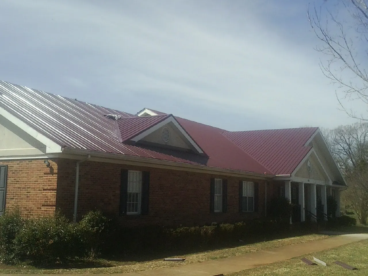 Red metal roof with gabled entries on a long brick building, from a Hail Damage Roof Repair job in Picture Rocks