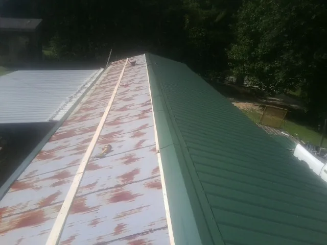 Old rusted panels beside newly installed green metal roofing — Wind Damage Roof Repair by Roofing Brothers in Picture Rocks