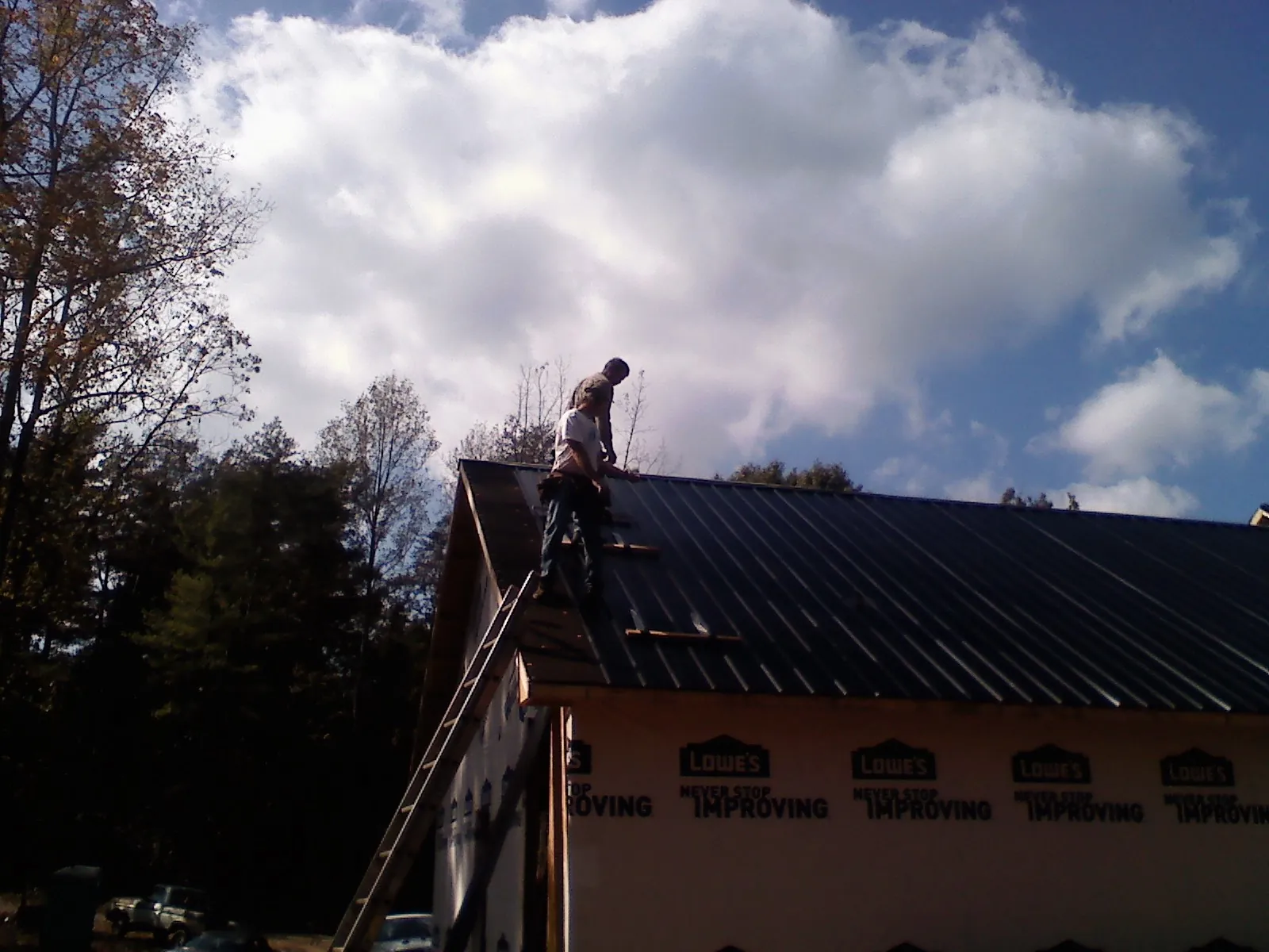 Roofer fastening dark metal panels high against a cloudy sky, from a Roof Inspection job in Picture Rocks