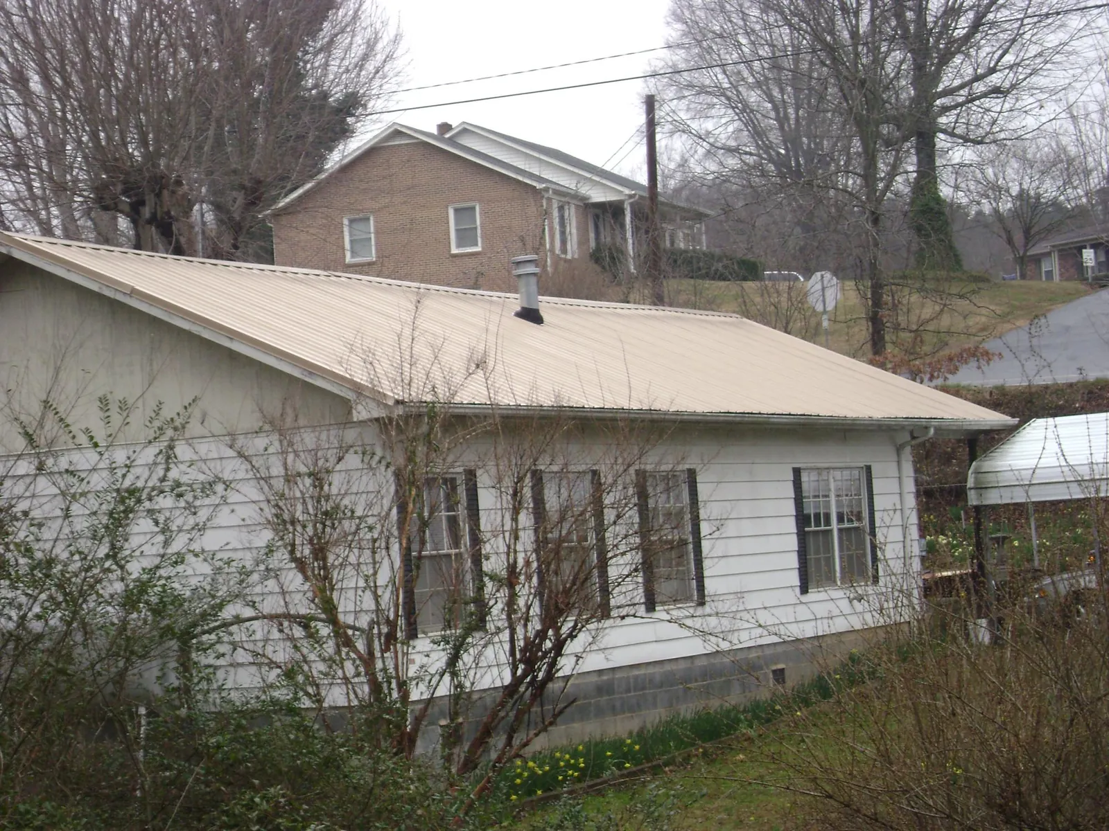 Tan metal roof on a white sided house set into a hillside — Commercial Roofing by Roofing Brothers in Picture Rocks